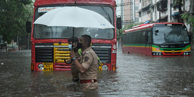 Polizist hilft Passanten während des Zyklons Tauktae in Indien über eine völlig überflutete Straße