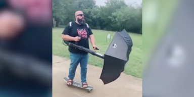 mann auf Skateboard mit Regenschirm